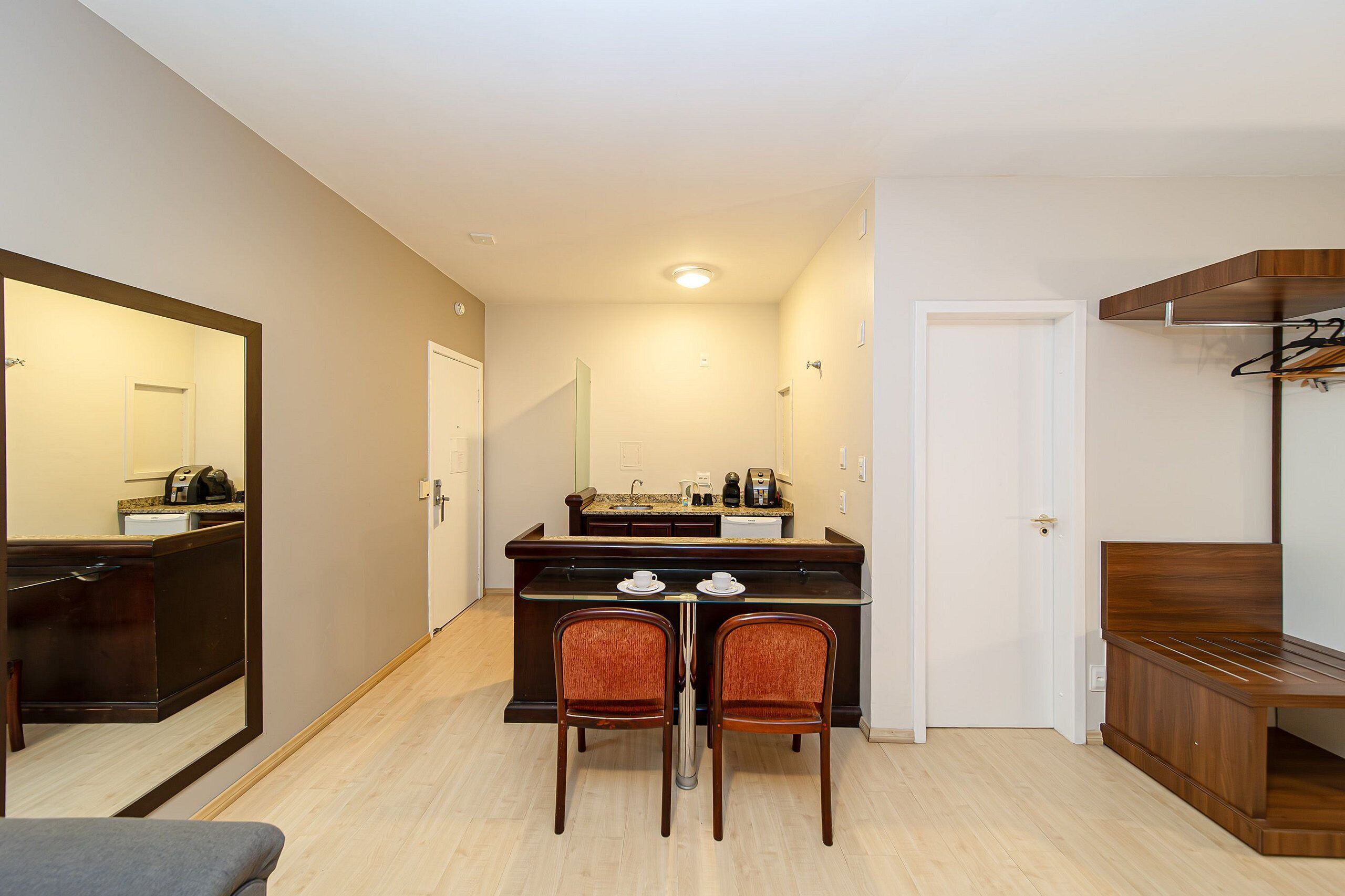 Quarto compacto com cozinha americana, área de refeições com duas cadeiras, um banco e um cabideiro.