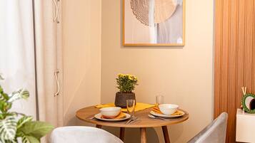 A dining area with a round table, two grey chairs, a potted plant, and a framed artwork on the wall.