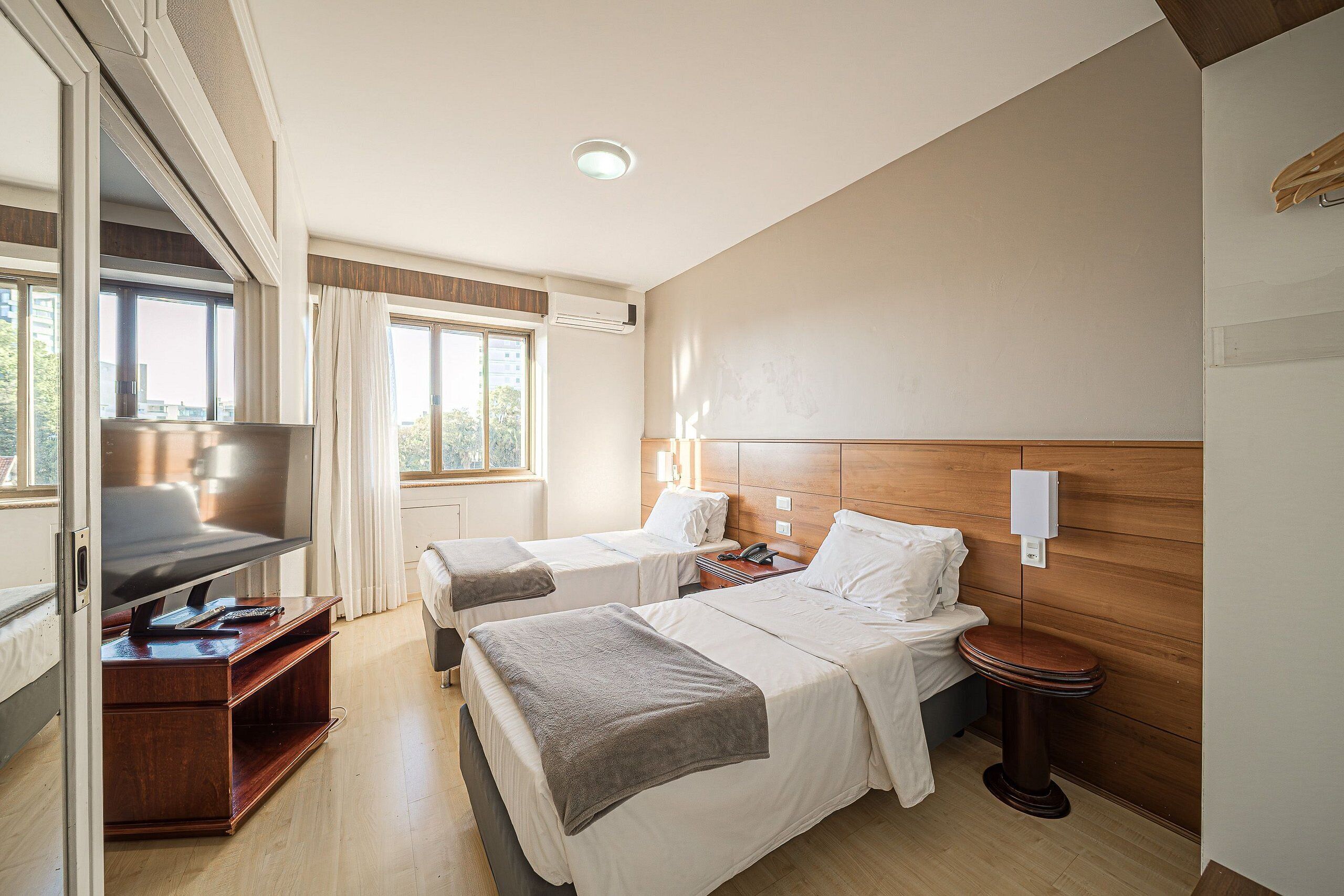 A hotel room with two beds, a TV, a desk, and a wooden headboard.