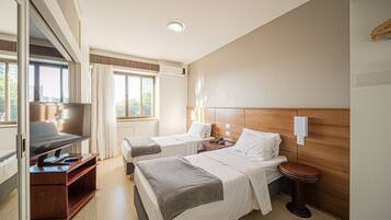 A hotel room with two beds, a TV, a desk, and a wooden headboard.