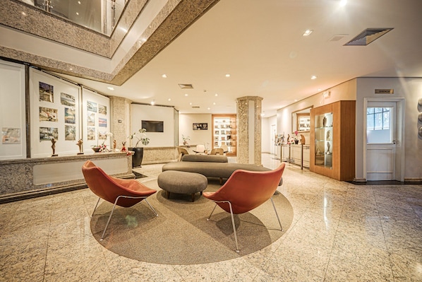 A lobby with a reception desk, seating area, and a large pillar. - Hotel Prinz (Joinville)