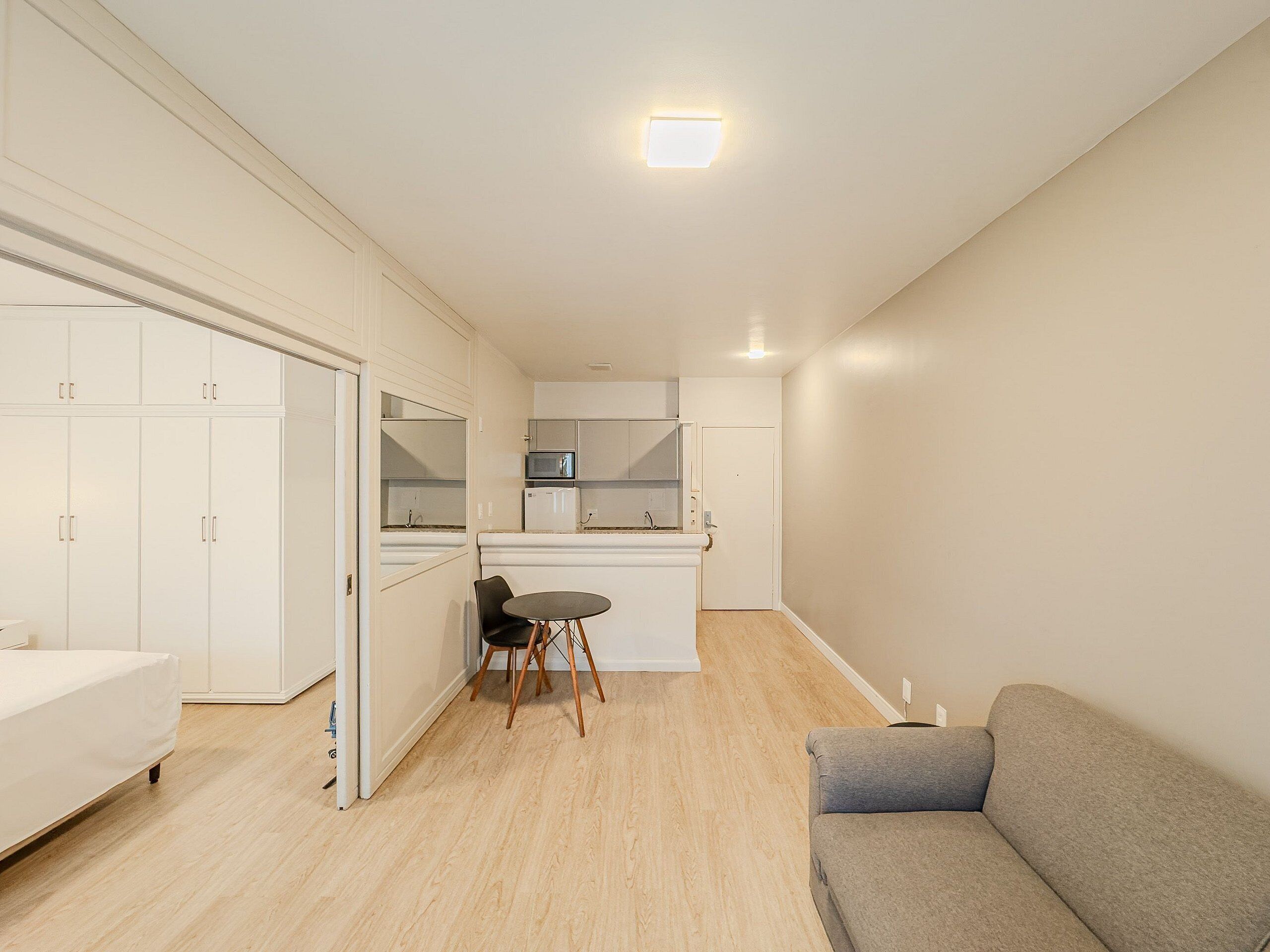 Um espaço de estar compacto com cozinha compacta, área de jantar com mesa e cadeiras, sofá e guarda-roupa.