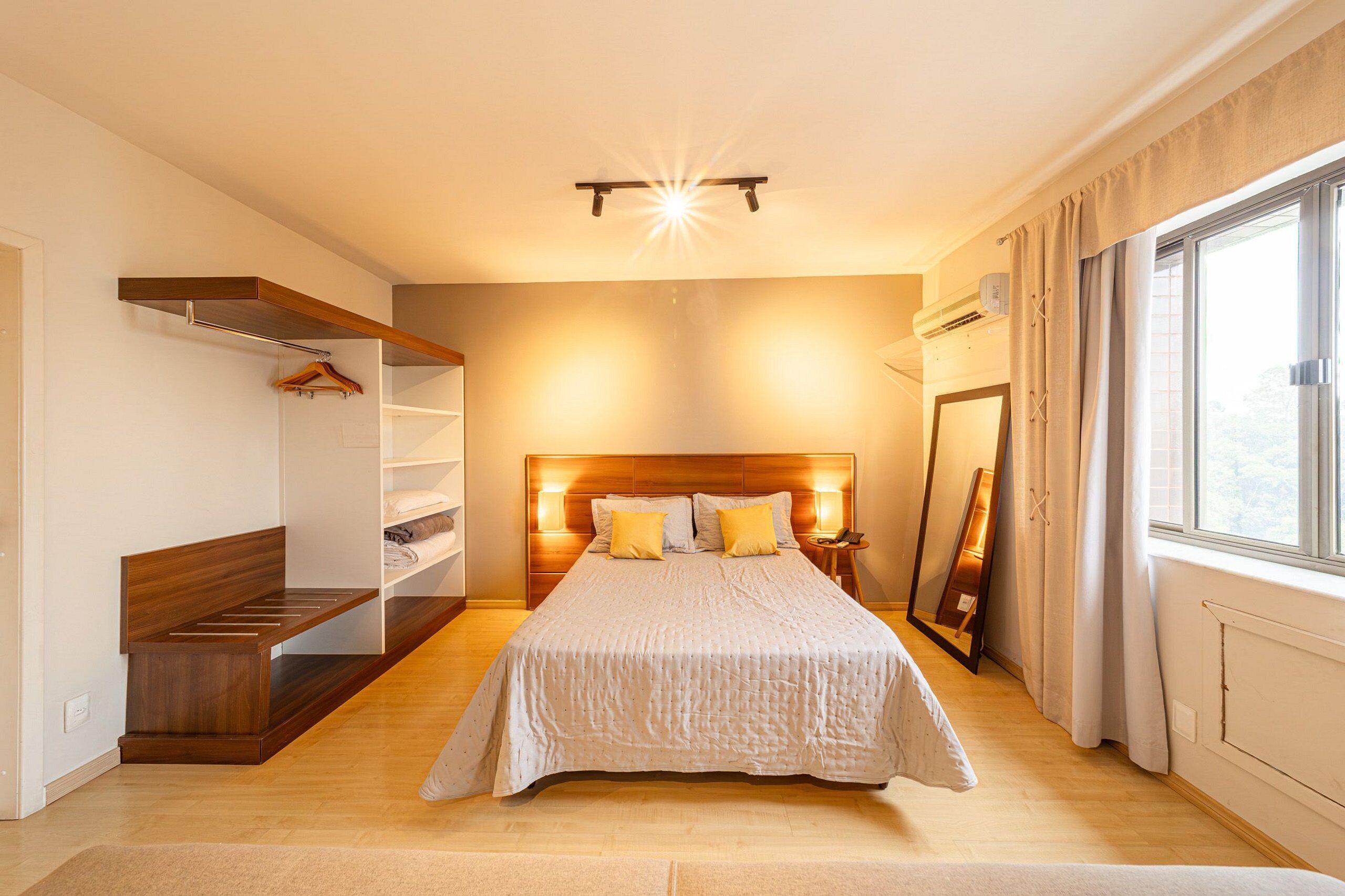 A bedroom with a bed, wooden headboard, bedside table, mirror, and built-in shelving.