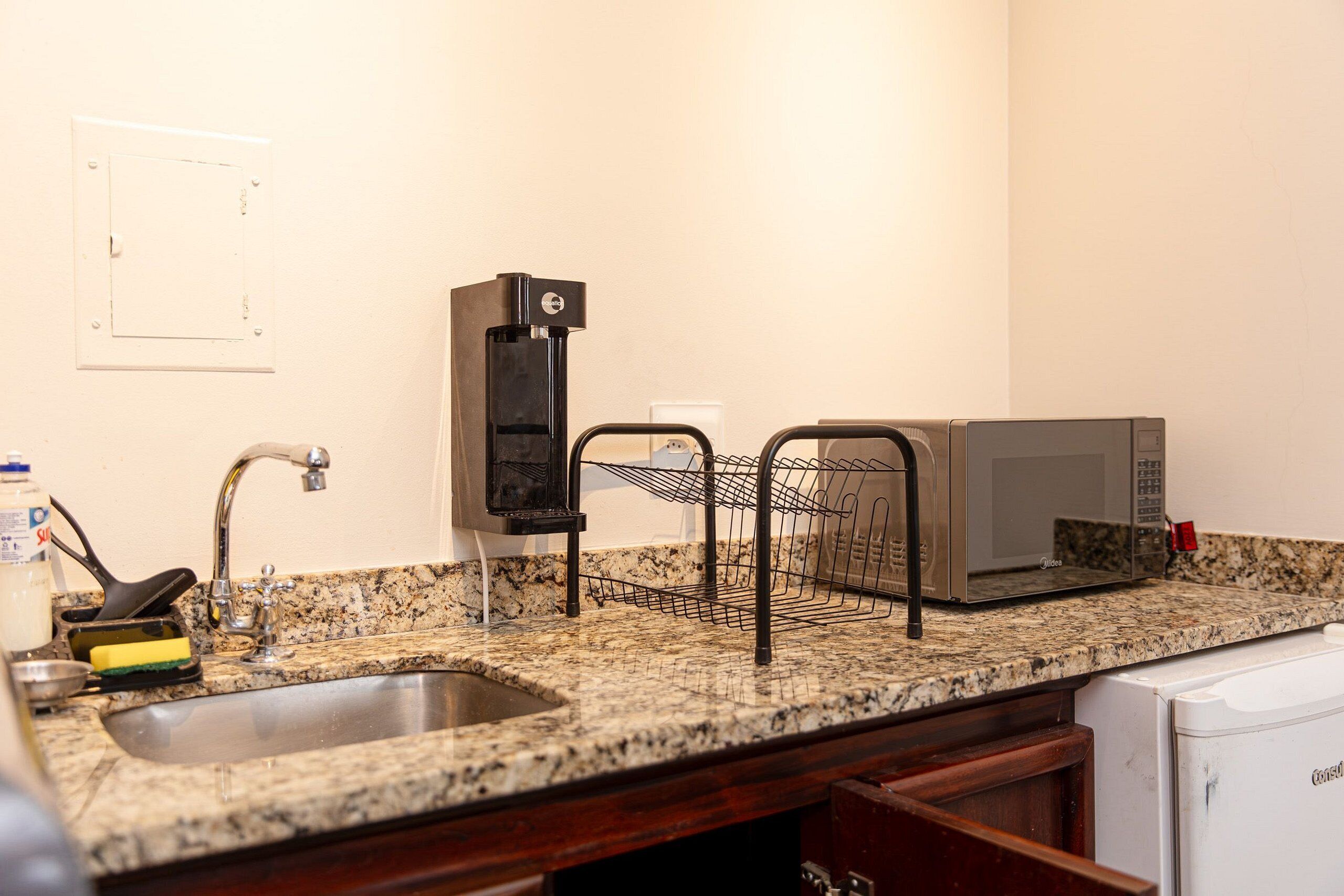 Una cocina con encimera de granito, pileta de acero inoxidable, cafetera, microondas y escurreplatos.