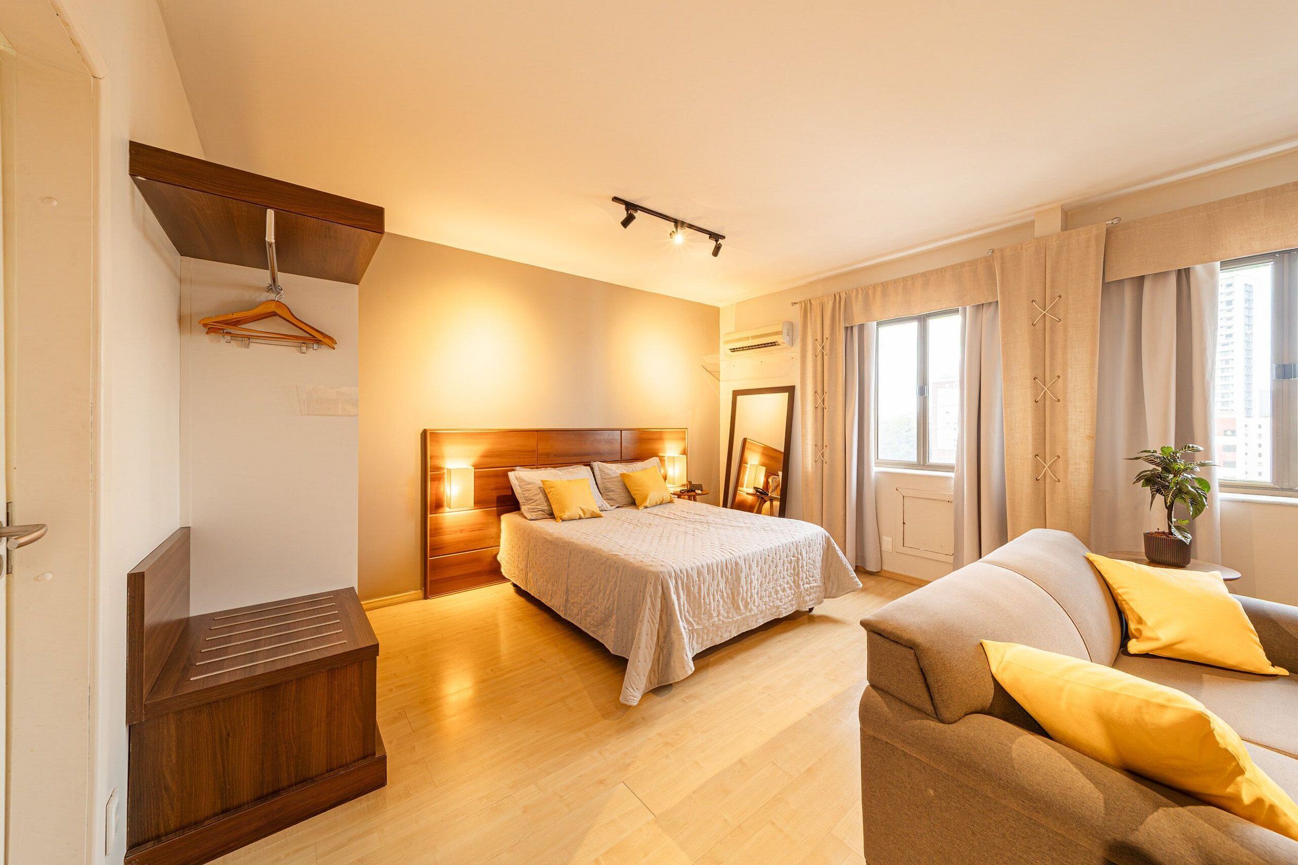 A bedroom with a bed, a sofa, a wooden bench, and a window with curtains.