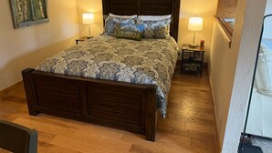 Ein Schlafzimmer mit einem hölzernen Bett, gemusterten Betttextilien, zwei Nachttischlampen, einem Nachttisch und einem Bild an der Wand.