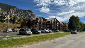 Ein Hotel vor einer Bergkulisse, mit mehreren Etagen und einem Parkplatz mit einigen Autos.