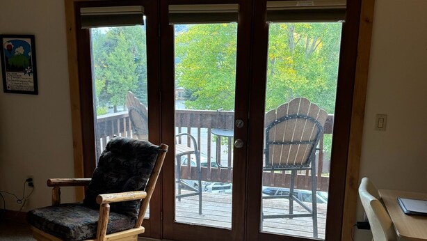 Ein Zimmer mit einem hölzernen Schaukelstuhl, einem Tisch und Blick durch eine Glastür auf eine Terrasse.
