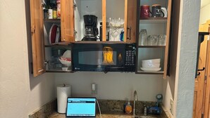 Eine kleine Küche mit Holzausstattung, einer eingebauten Mikrowelle, einer Kaffeemaschine und einem Laptop auf der Arbeitsplatte.