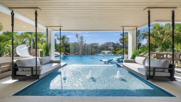 Uma área de piscina com escorrega, várias áreas de estar com almofadas, e vista para uma cascata ao fundo.