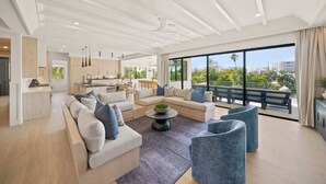 Uma sala de estar moderna com um conjunto de sofás, uma mesa de centro e vista para a cidade através de grandes janelas.