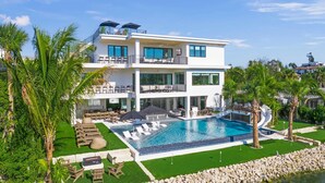 Uma casa moderna com dois andares, piscina grande, móveis de exterior e palmeiras.