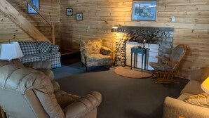 Interior acogedor de una cabaña de troncos con chimenea de piedra, sillones de cuero y un sofá a cuadros.
