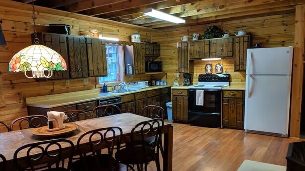 Una cocina estilo cabaña de madera con una mesa, sillas, un refrigerador y armarios de madera.
