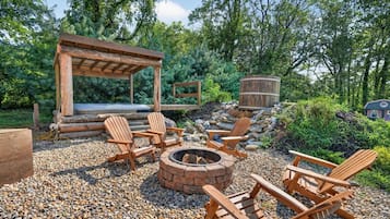 Un espacio al aire libre con sillas Adirondack, un brasero y una pérgola de madera.