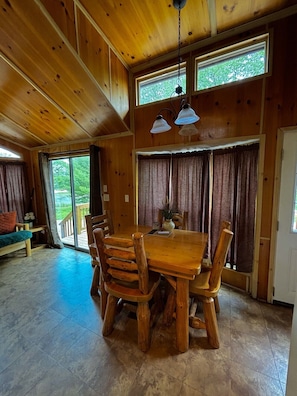 A wooden dining room with a large table and chairs, a hanging light fixture, and a view through the windows. - Waterfront Bourbon Barrel Cabin (Indianapolis)