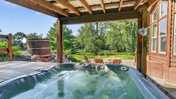Un jacuzzi con terraza de madera, rodeado de mobiliario exterior y una cabaña de madera.