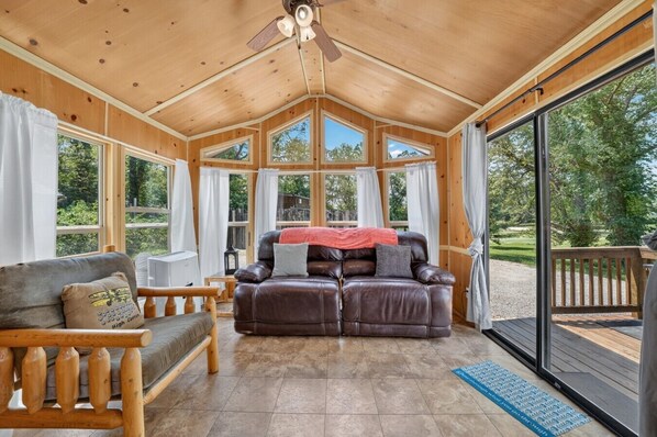 Een gezellig interieur van een chalet met een leren bank, houten meubels en grote ramen met uitzicht op de omgeving.
