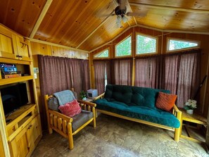 Interior de una cabaña de madera con sofá, sillón, televisor y cortinas.
