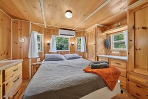 Une chambre dans une cabane en bois, avec un lit, deux fenêtres, un radiateur et une petite table.