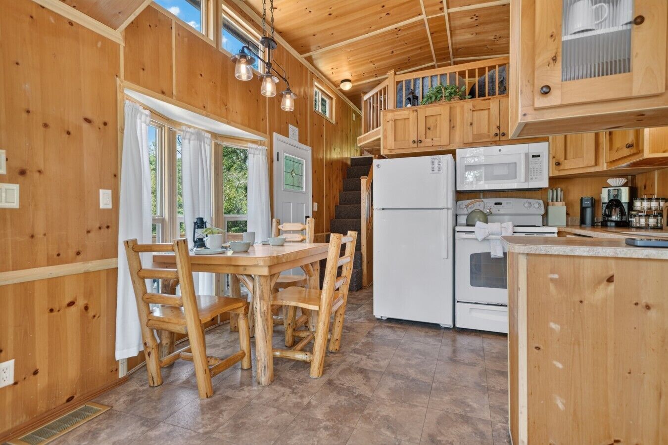 A wooden interior with a dining table, chairs, a refrigerator, a microwave, and a stove.