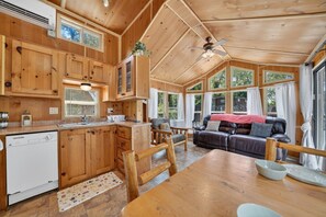 A wooden cabin interior with a kitchen, dining area, and a living room with a sofa and chairs. - Little Lantern Cabin (Indianapolis)