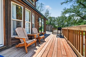 A wooden deck with two Adirondack chairs and a grill, overlooking a gravel path and trees. - Little Lantern Cabin (Indianapolis)