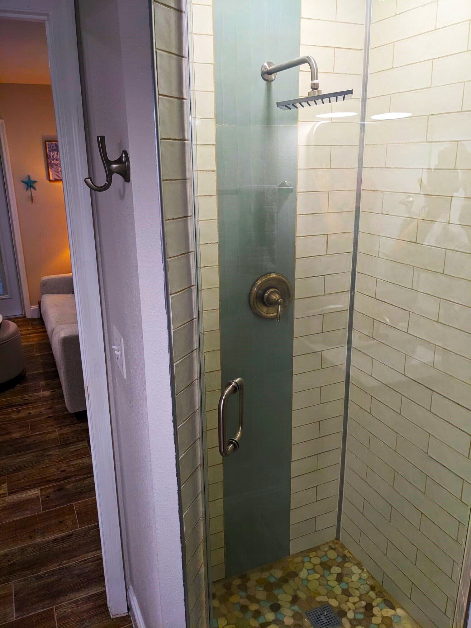 A glass-enclosed shower with a tiled floor, a door with a handle, and a showerhead.