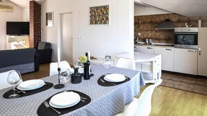 A dining area with a table set for four, a TV in the background, and a kitchen with modern appliances.