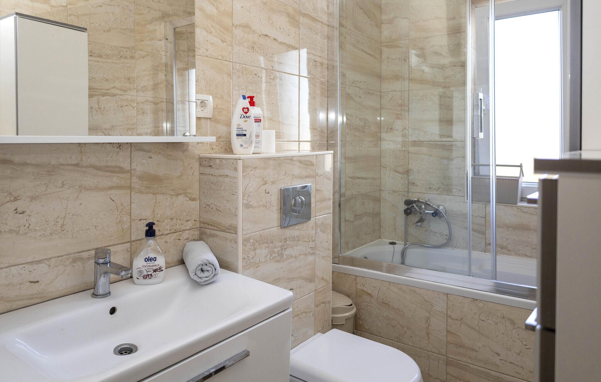 A bathroom with a sink, toilet, and shower. There are toiletries on the sink and a towel on the floor.