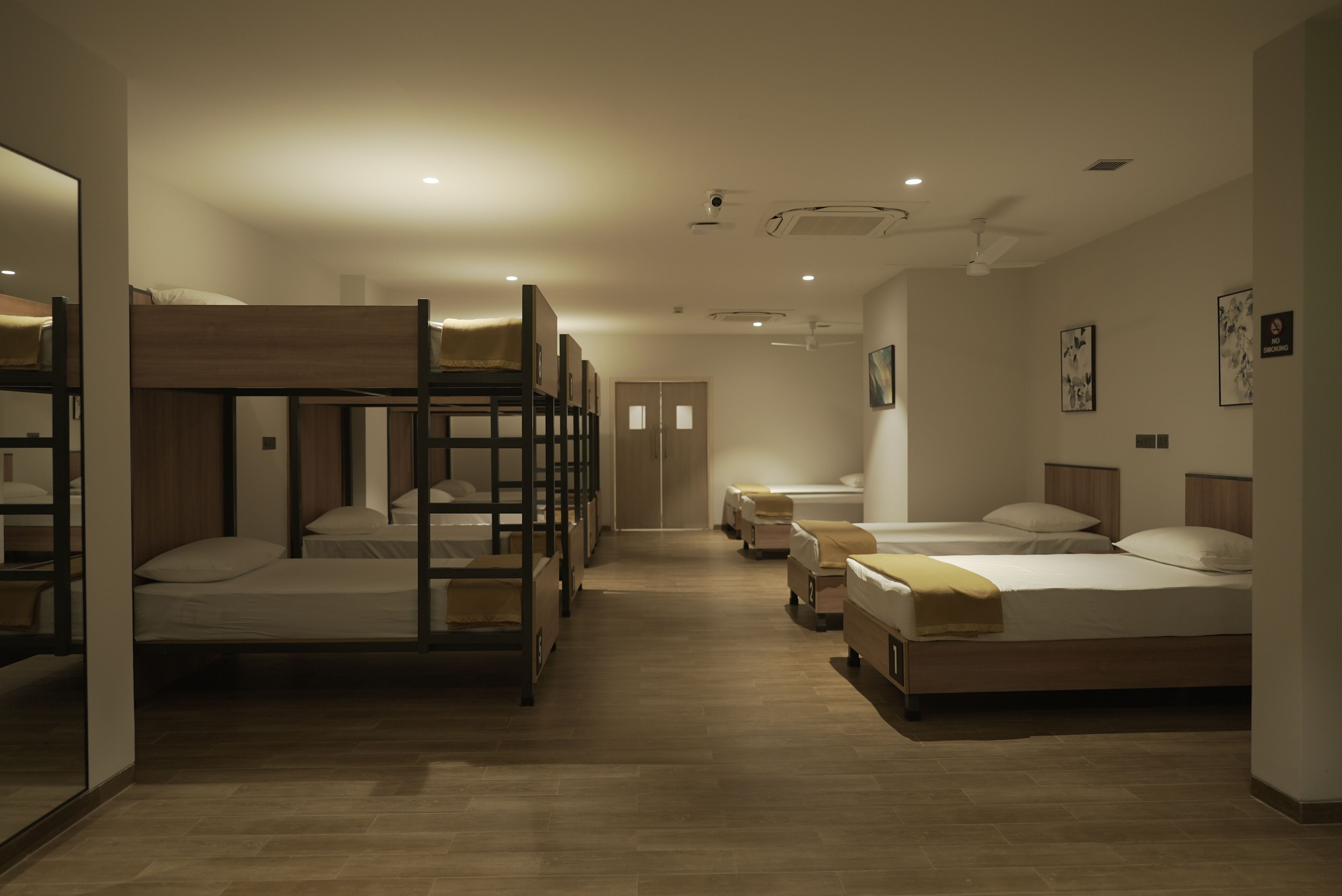 A hotel room with bunk beds, a wooden floor, and a door leading to another room.