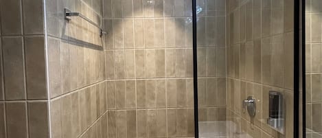 Un baño moderno con ducha de vidrio, lavamanos blanco y azulejos color beige.