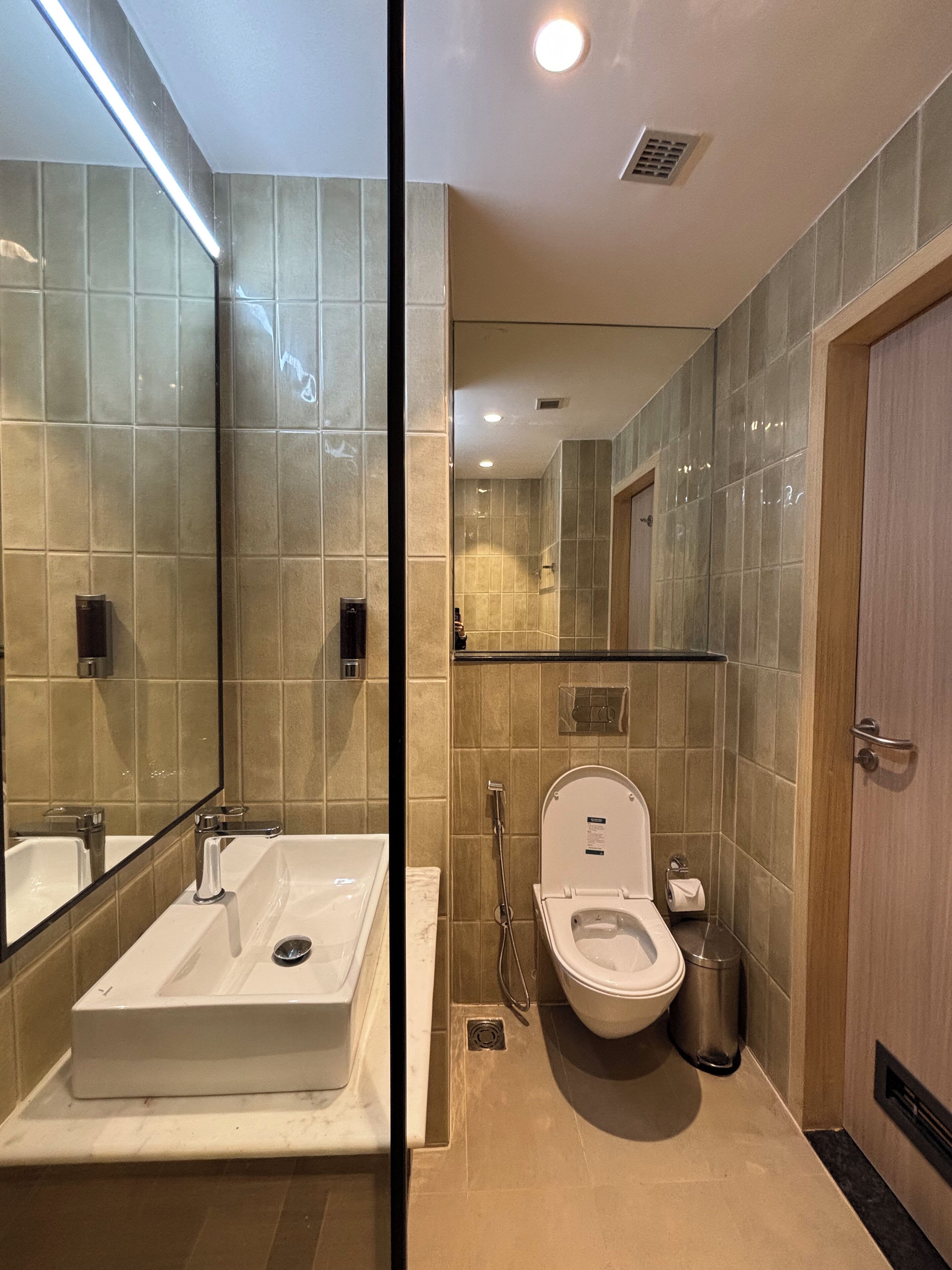 A modern bathroom with a large mirror, a sink, a toilet, and a shower.