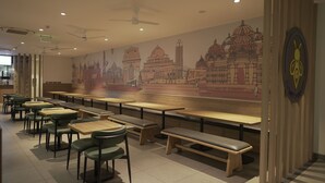 A restaurant interior with multiple tables and chairs, a mural of Indian architecture, ceiling fans, and recessed lighting. - Round D Clock (New Delhi)
