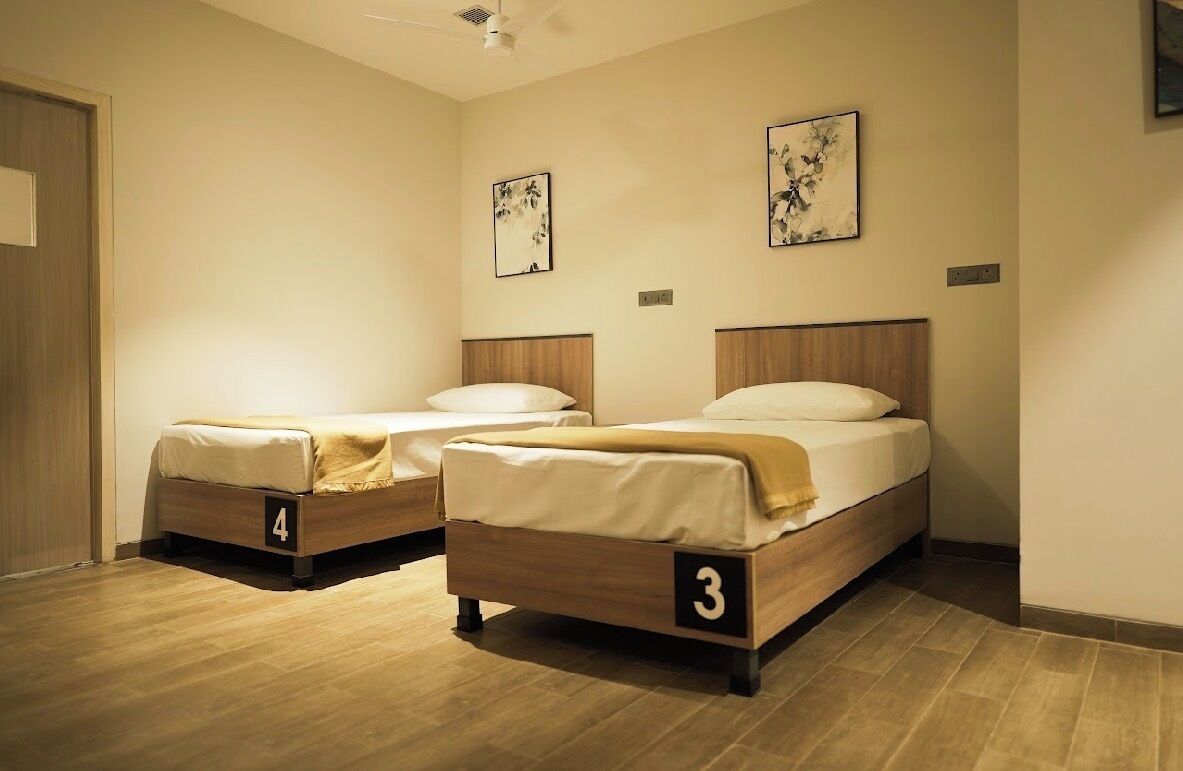 A hotel room with two beds, each marked with a number, wooden flooring, and artwork on the walls.