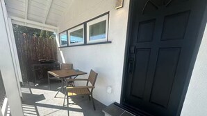 A covered patio with a table and chairs, a black door, and a window above the door. - Monterey Bay Hideaway (Seaside)