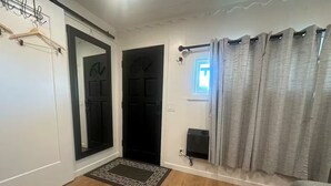 A room with wooden flooring, a black door, a window with curtains, and a small black speaker on the wall. - Monterey Bay Hideaway (Seaside)