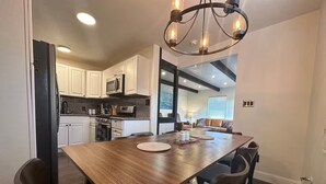 Una cocina moderna con armarios blancos, una mesa de comedor de madera y una araña.