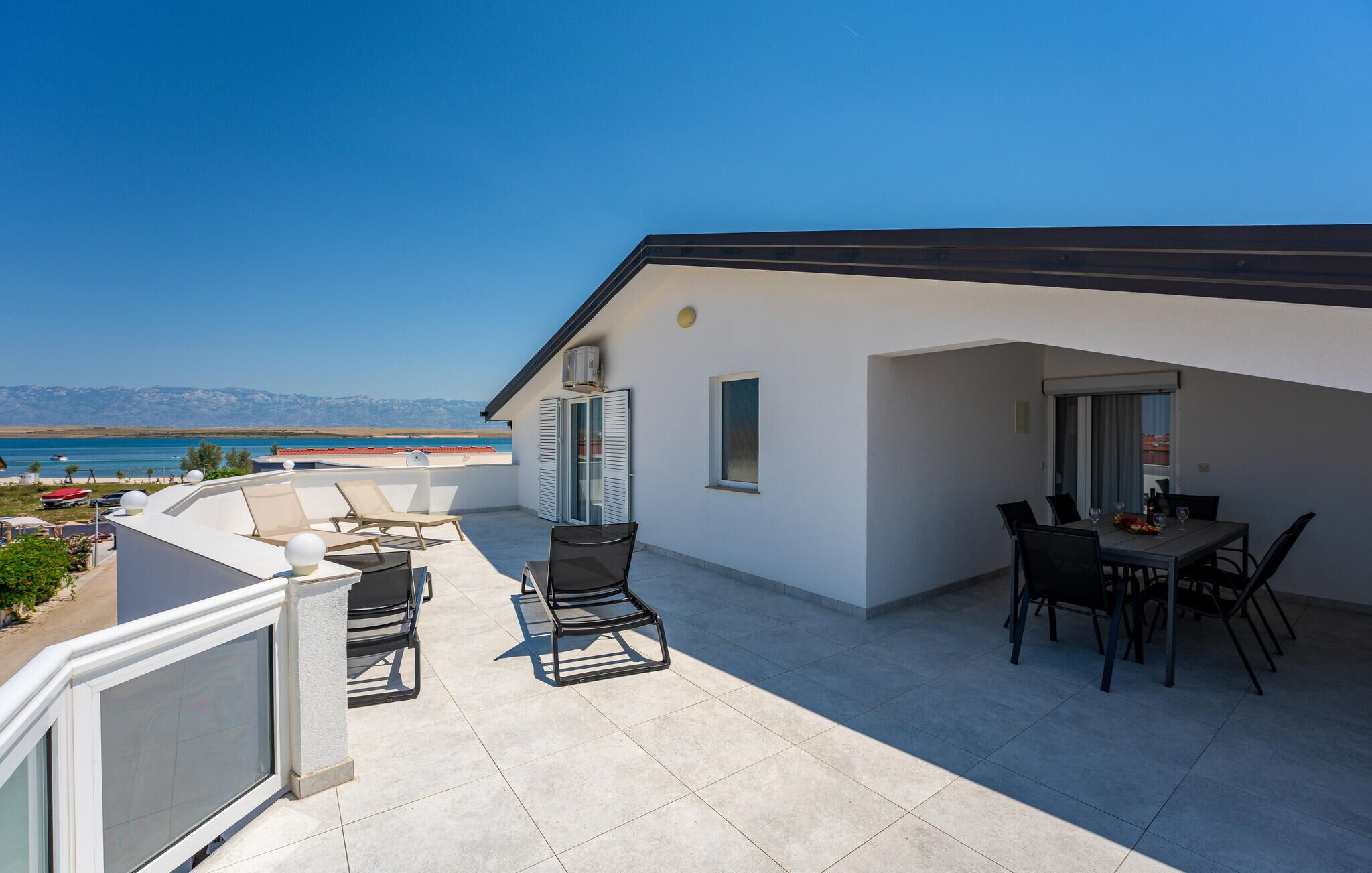 Ein Balkon mit Außenmöbeln, einem Essbereich und Blick aufs Meer.