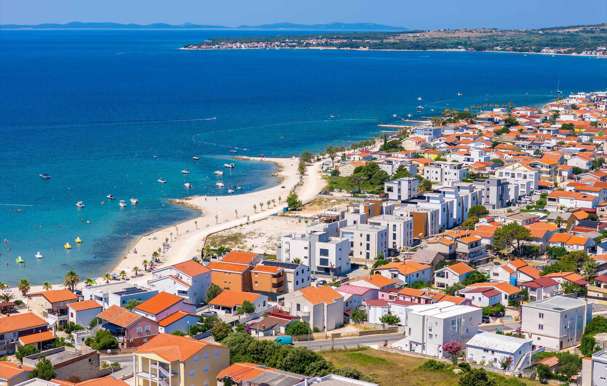 A coastal town with a beach, residential buildings, and boats on the water.