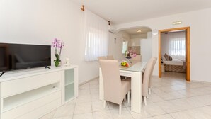 Un soggiorno moderno con una TV a schermo piatto, un tavolo da pranzo con sedie, un divano bianco e una zona cucina visibile attraverso un arco.