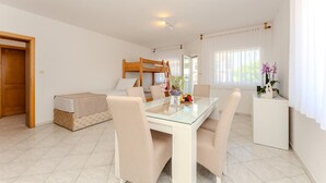 Una camera d'albergo con un letto a castello, un tavolo da pranzo in vetro con sedie, un angolo cottura e una finestra con tende.