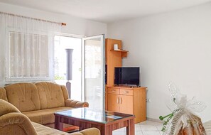 A living room with a sofa, a glass-top coffee table, a wooden cabinet with a television, and a window with curtains.