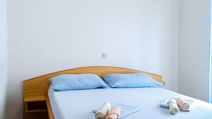 Un lit simple avec une tête de lit en bois, deux oreillers bleu clair et des serviettes enroulées posées sur un couvre-lit bleu clair.