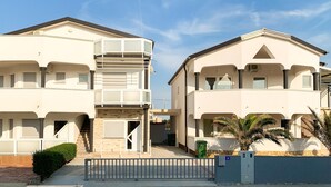 Un immeuble résidentiel de deux étages doté d’un balcon, d’une entrée sécurisée et d’un petit jardin agrémenté d’un palmier.