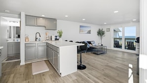 Une cuisine moderne dotée d’un îlot central, un coin repas avec vue et un salon avec balcon.