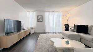 A modern living room with a flat-screen TV, a sofa, a coffee table, and a large window with sheer curtains. - #11 Modern 2-BR sanctuary walk to shops & beach (Santa Monica)