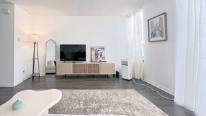 A modern living room with a flat-screen TV, a floor lamp, a large mirror, and a framed picture on the wall. - #11 Modern 2-BR sanctuary walk to shops & beach (Santa Monica)