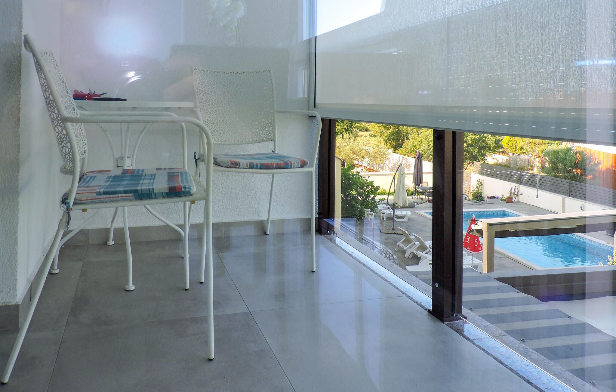 Een balkon met twee witte stoelen, waarvan één met een geruit kussen en de andere met een gestreept kussen. Op een klein tafeltje staat een rood voorwerp.