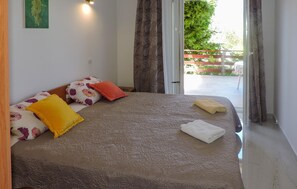 Ein Schlafzimmer mit Bett, Kissen, Decke, Handtuch und Blick auf einen Außenbereich mit Holzzaun und Grünflächen.